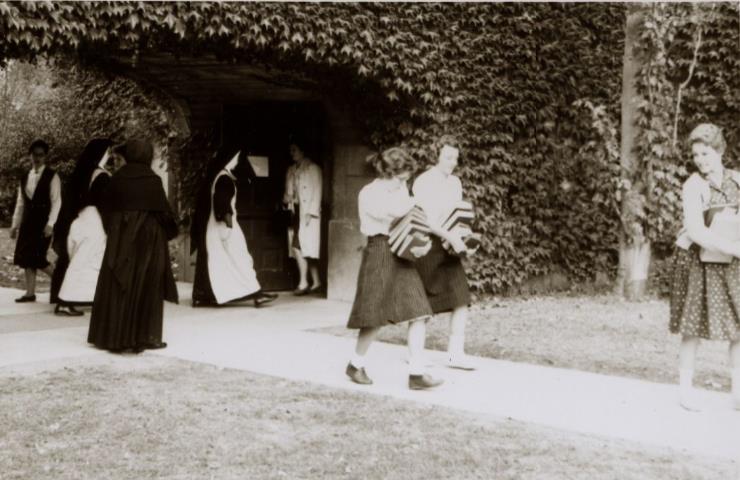 CSJ sisters and students carrying books under the archway by the chapel