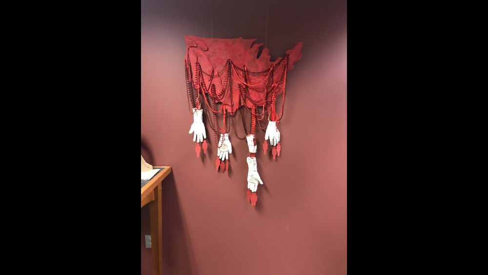 REDress Project example response: a scrap of red cloth with red bead neckalces and white gloves hanging off of it